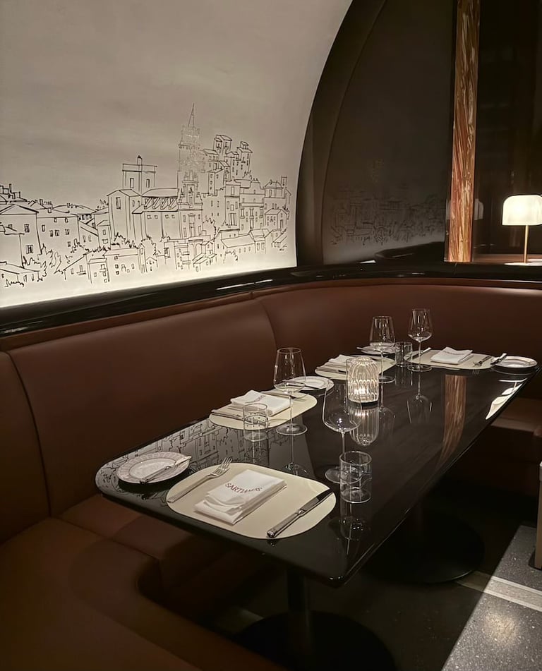 An upscale restaurant dining booth with burgundy seating, place settings, water glasses, and a cityscape illustration on the illuminated wall