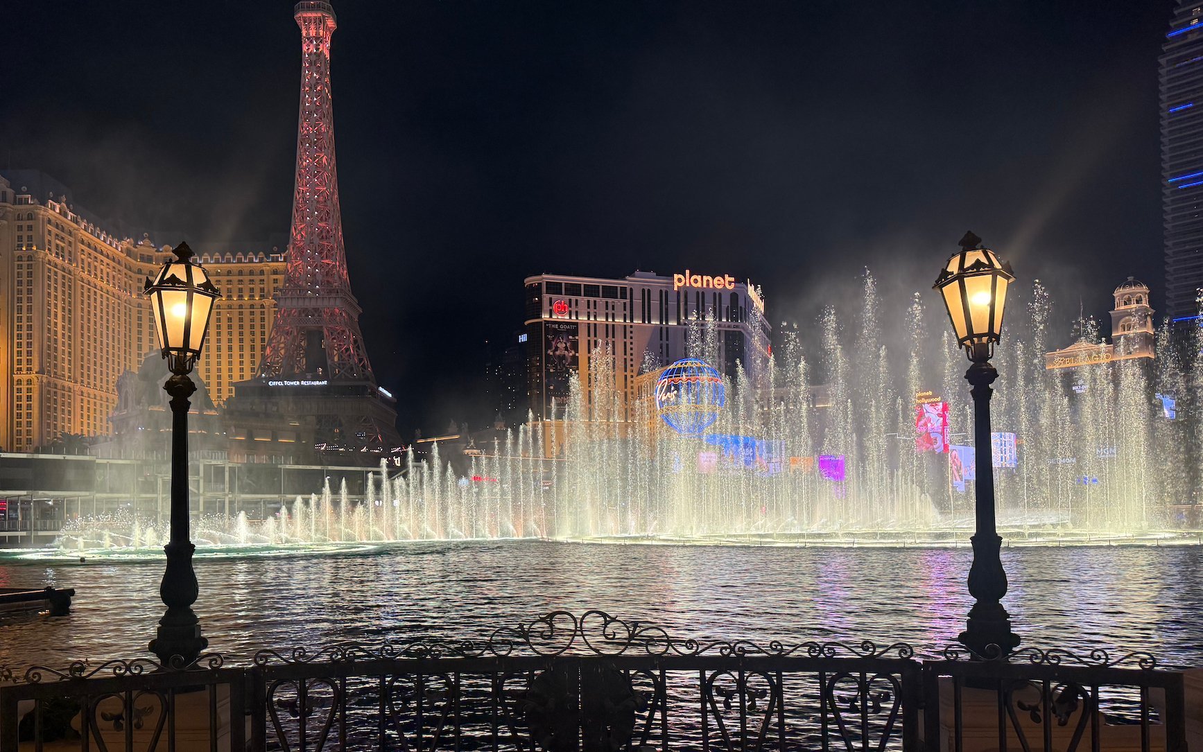 Nighttime view of illuminated fountains with Eiffel Tower replica and vintage street lamps in Las Vegas