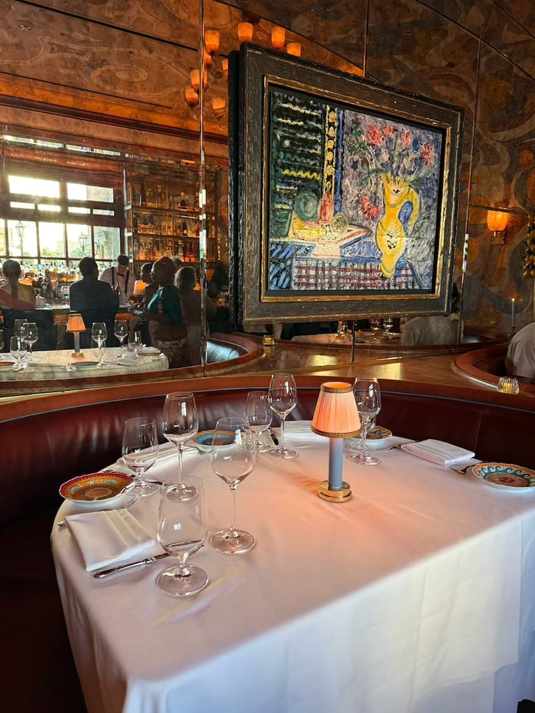 Upscale restaurant dining table with white tablecloth and place settings, red leather banquette seating, and framed artwork on wall