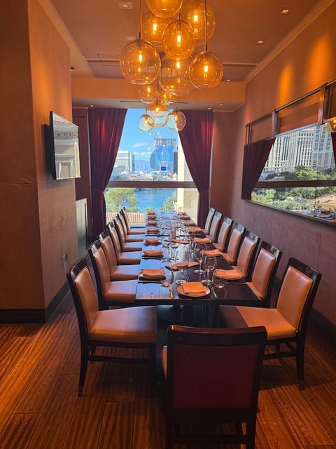 Upscale private dining room with long table, orange leather chairs, amber glass pendant lights, burgundy curtains, and city skyline view