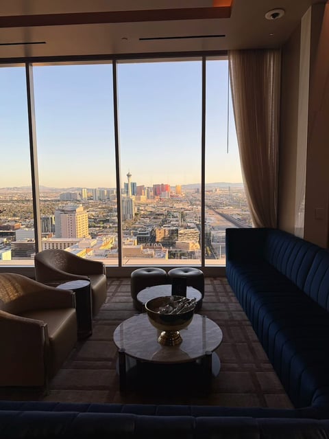 Modern high-rise lounge with leather and blue seating, circular table, and panoramic city skyline view through floor-to-ceiling windows