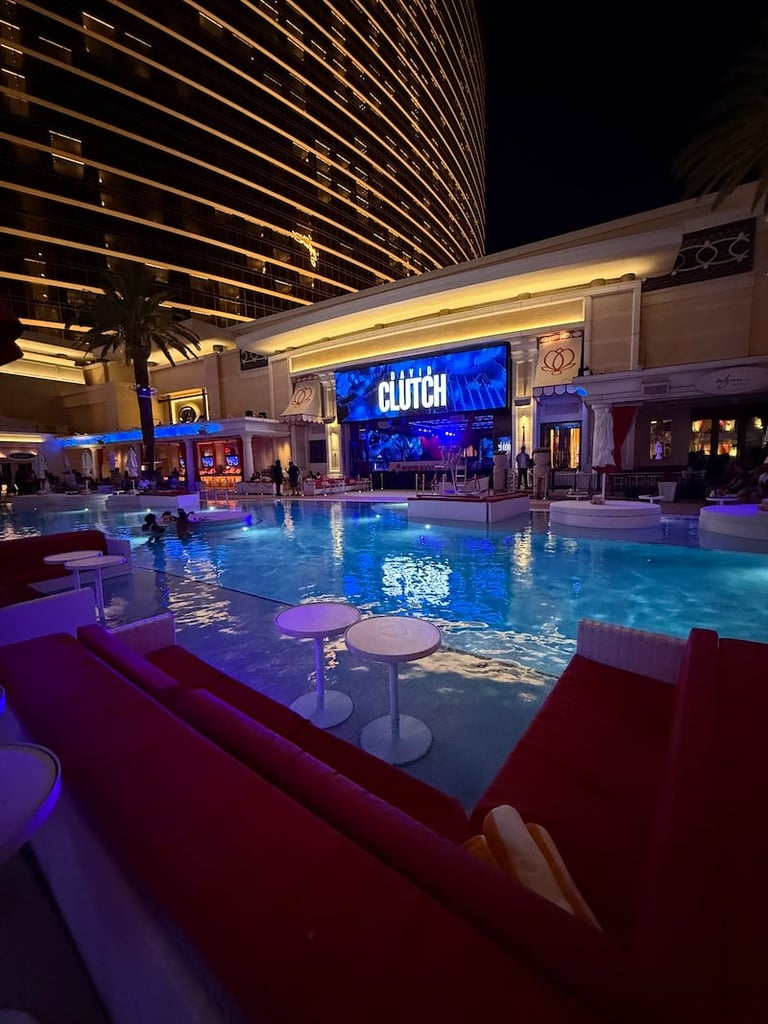 Modern nightclub with illuminated blue swimming pool, neon CLUTCH sign, lounge seating, and tall lit building at night