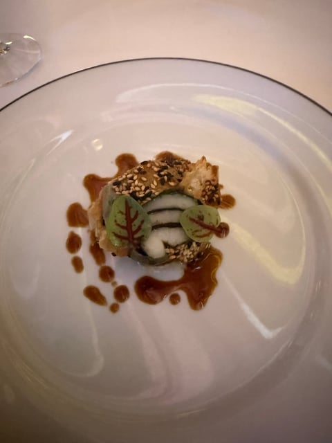Gourmet plated dish with seared scallop topped with nuts, sliced apple, microgreens, and caramel sauce on white plate