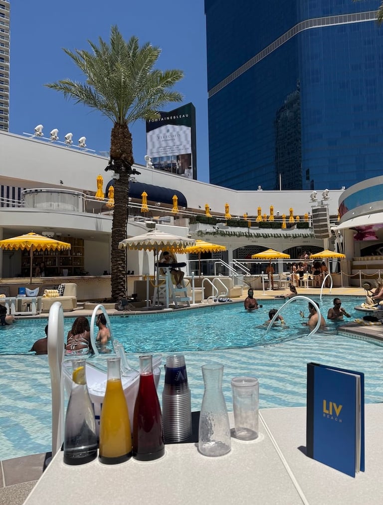 Poolside beverage setup at a luxury resort with blue water, yellow umbrellas, palm tree, and modern high-rise buildings in background