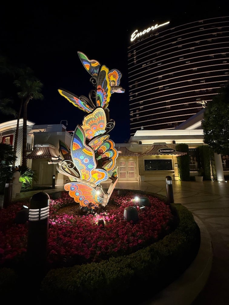 Illuminated colorful butterfly sculpture at night outside Encore hotel with red landscaping and lit palm trees