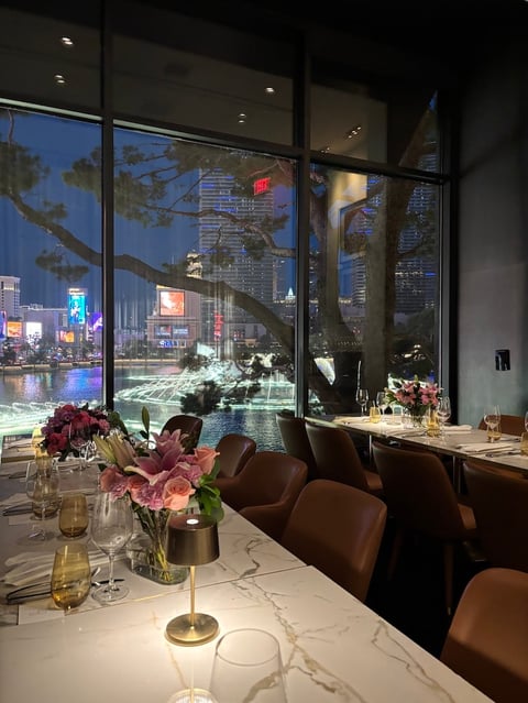 Upscale restaurant dining room with floor-to-ceiling windows overlooking illuminated city skyline at night