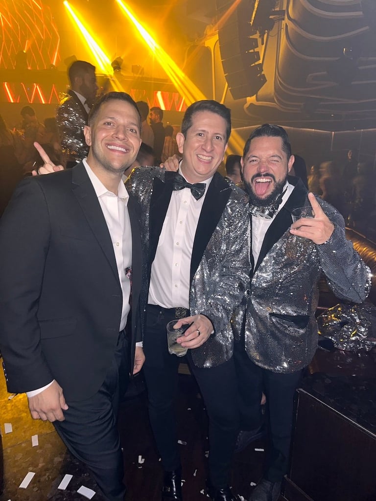 Three men in formal attire posing at a nightclub with golden neon lights in the background