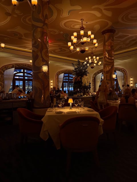 Elegant upscale restaurant dining room with ornate ceiling, chandeliers, and candlelit tables set for fine dining