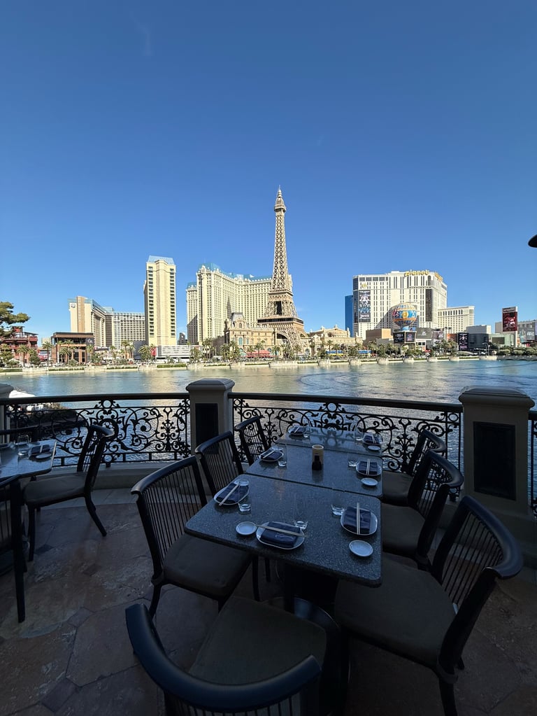 Outdoor dining terrace overlooking Las Vegas skyline with Eiffel Tower replica and casino buildings across the water