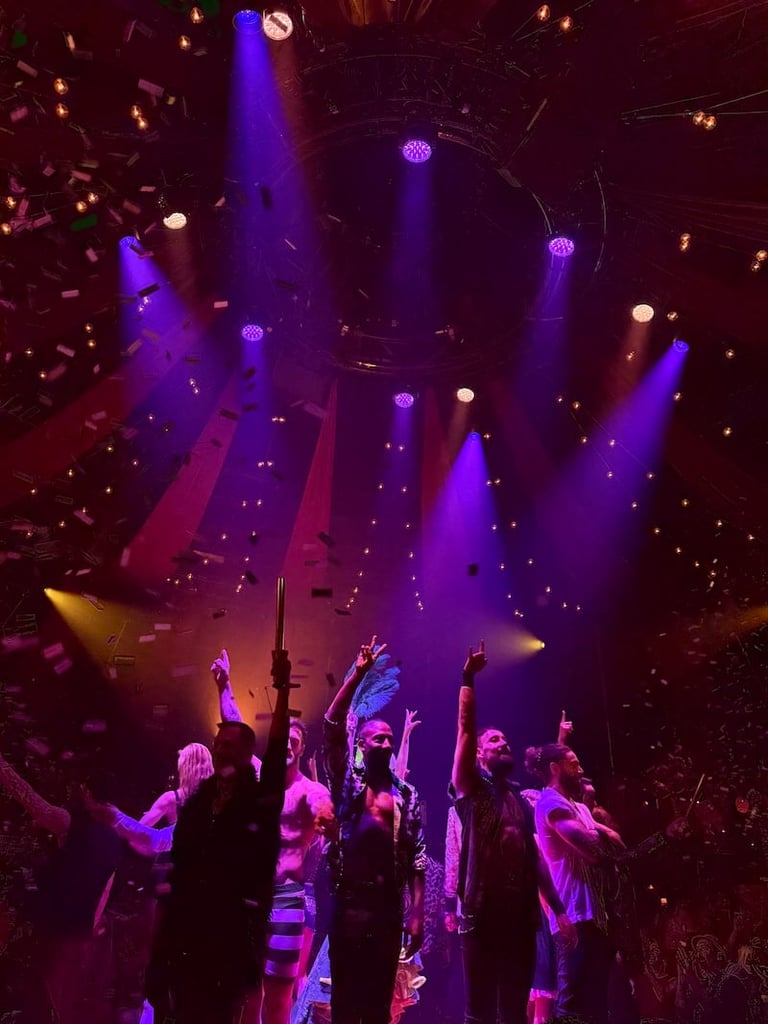 Concert crowd under purple and blue stage lights with raised hands and colorful beams illuminating the dark venue.
