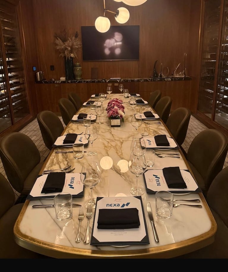 Elegant formal dining room with long marble table set for a business dinner, featuring place settings, pendant lights, and wood-paneled walls.