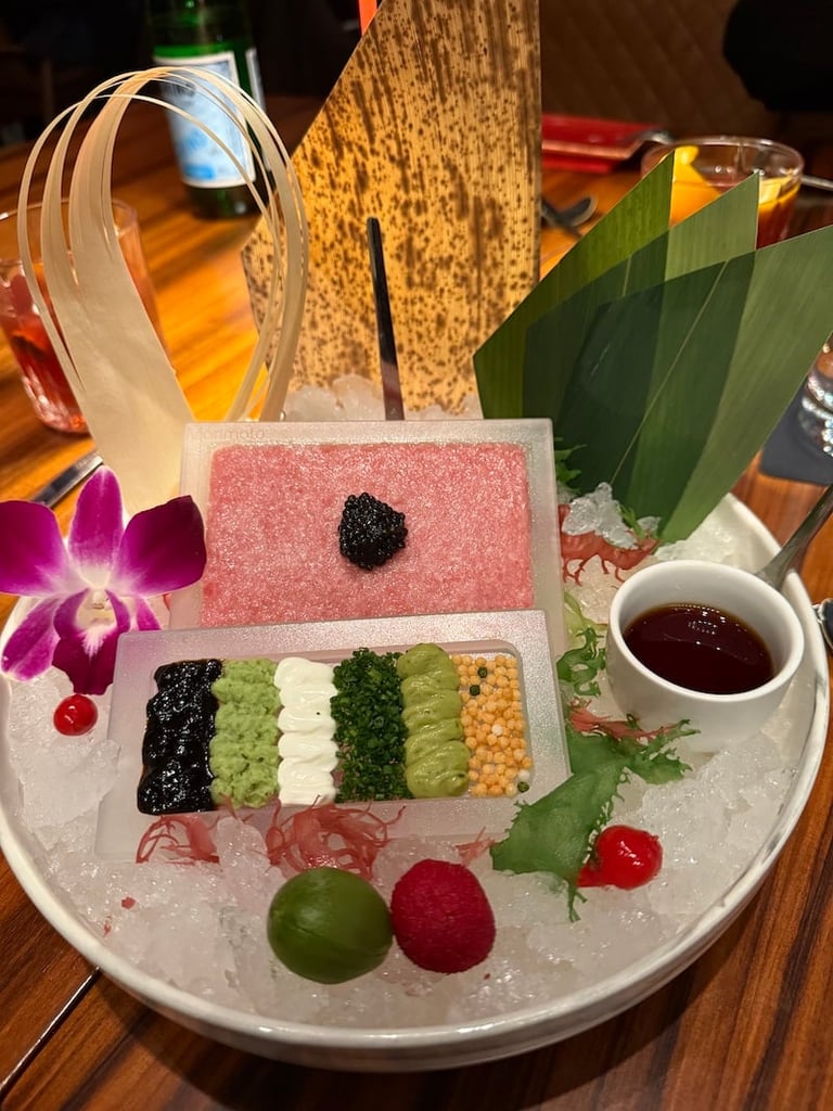 Elegant plated dessert with colorful mochi strips, pink frosted cake, fresh fruits, and garnishes arranged artfully on ice.